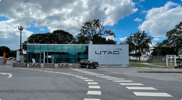 The modern entrance gate of a company premises featuring a glass guardhouse and a sign displaying "UTAC" under a cloudy sky.