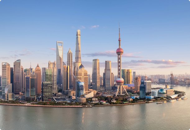 A stunning skyline of Shanghai featuring numerous skyscrapers and the Oriental Pearl Tower along the Huangpu River under clear weather and a blue sky.