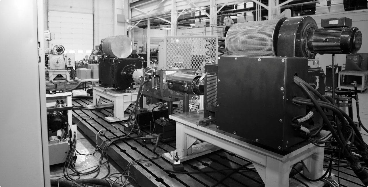 A black and white image of a laboratory or research facility with complex machinery and optical devices mounted on benches. Many cables, lenses, and metallic components are visible, suggesting precision measurements or experiments.