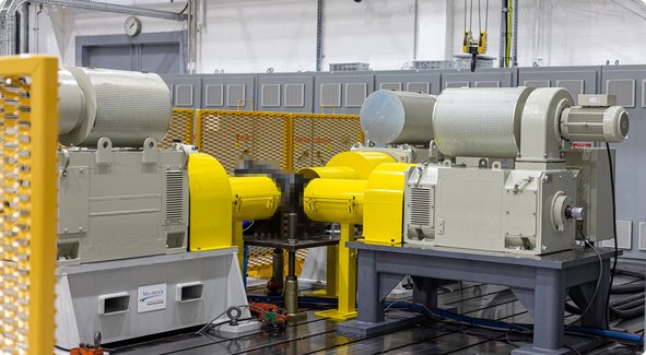 Two large, gray industrial machines with yellow safety guards stand in a factory hall.