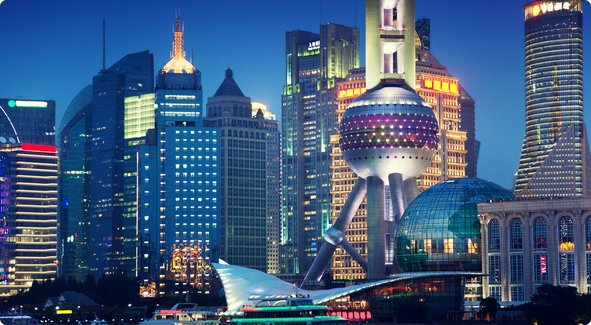 A nighttime skyline of a modern metropolis featuring numerous illuminated skyscrapers and a prominent, futuristic-looking building in the center.