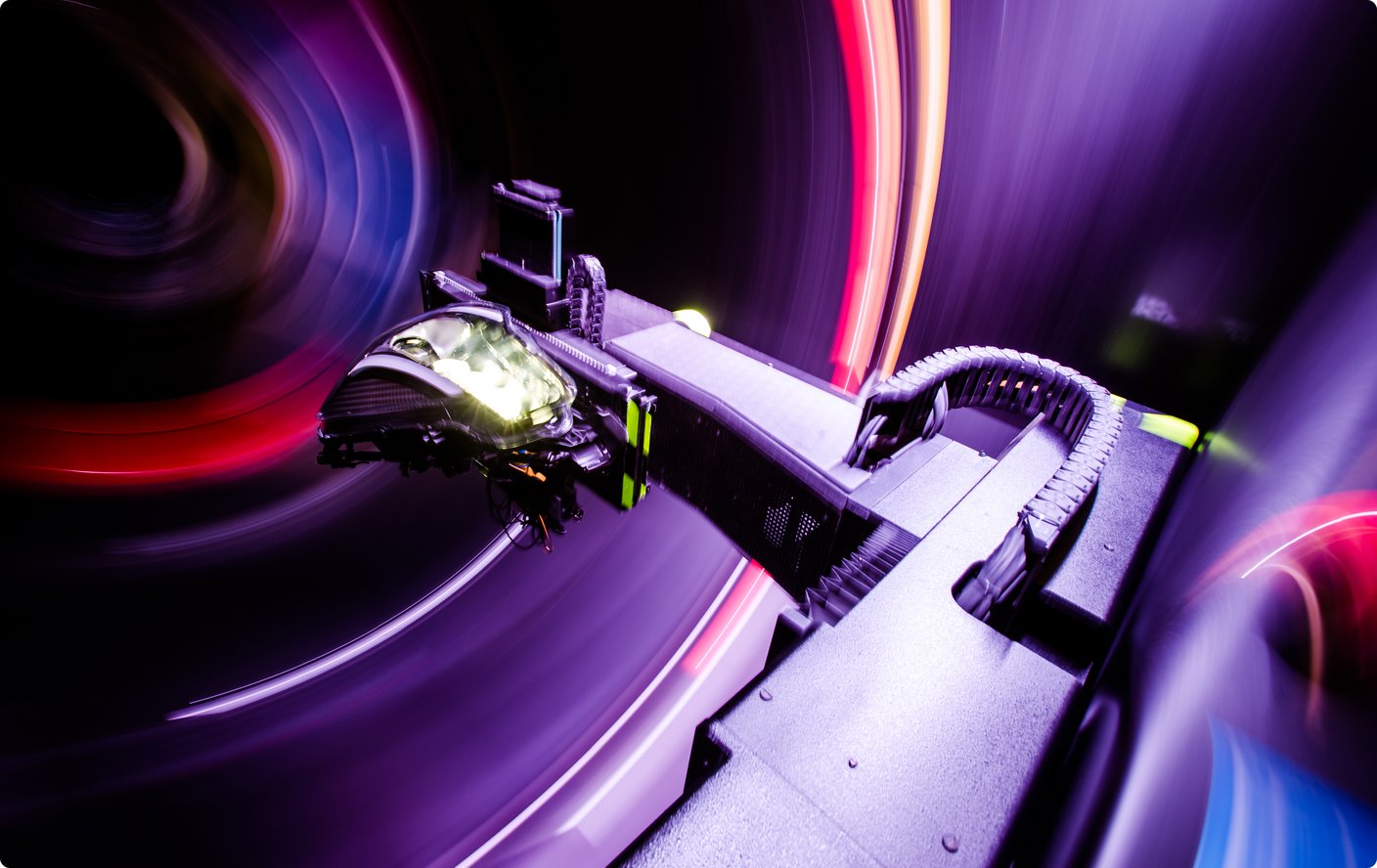 A close-up of part of a machine or device with blurry, glowing purple and red light trails in the background, suggesting motion.